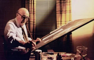 O cartunista Will Eisner, criador do Spirit, sentado trabalhando em sua prancheta de desenho com pincel e tinta em um estúdio com pouca luz.